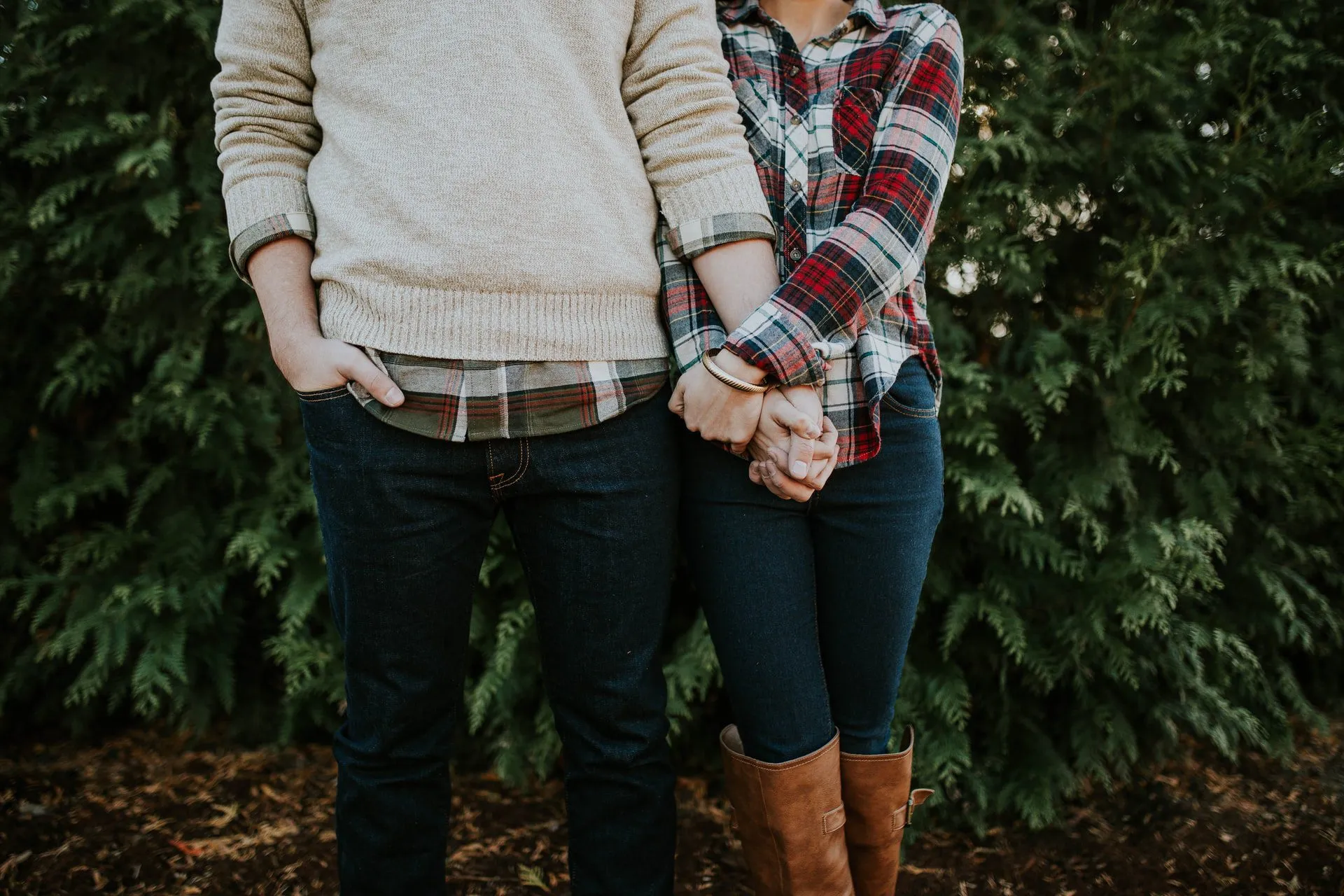 Couple holding hands in casual attire against a lush green background.