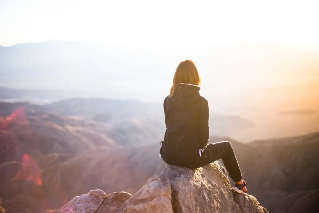 Woman sitting on a mountain rock gazing at a scenic sunrise.