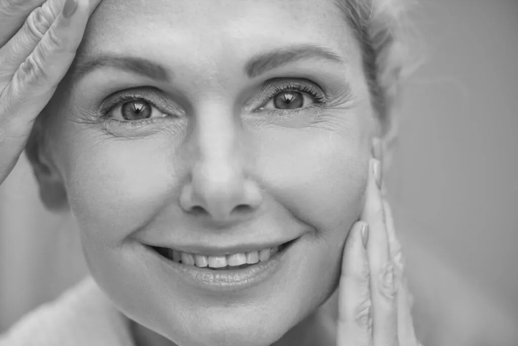 Close-up of a smiling woman touching her face, highlighting smooth skin and youthful appearance.