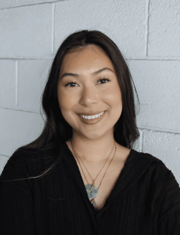 Smiling woman with long dark hair, wearing a black top and layered necklaces.