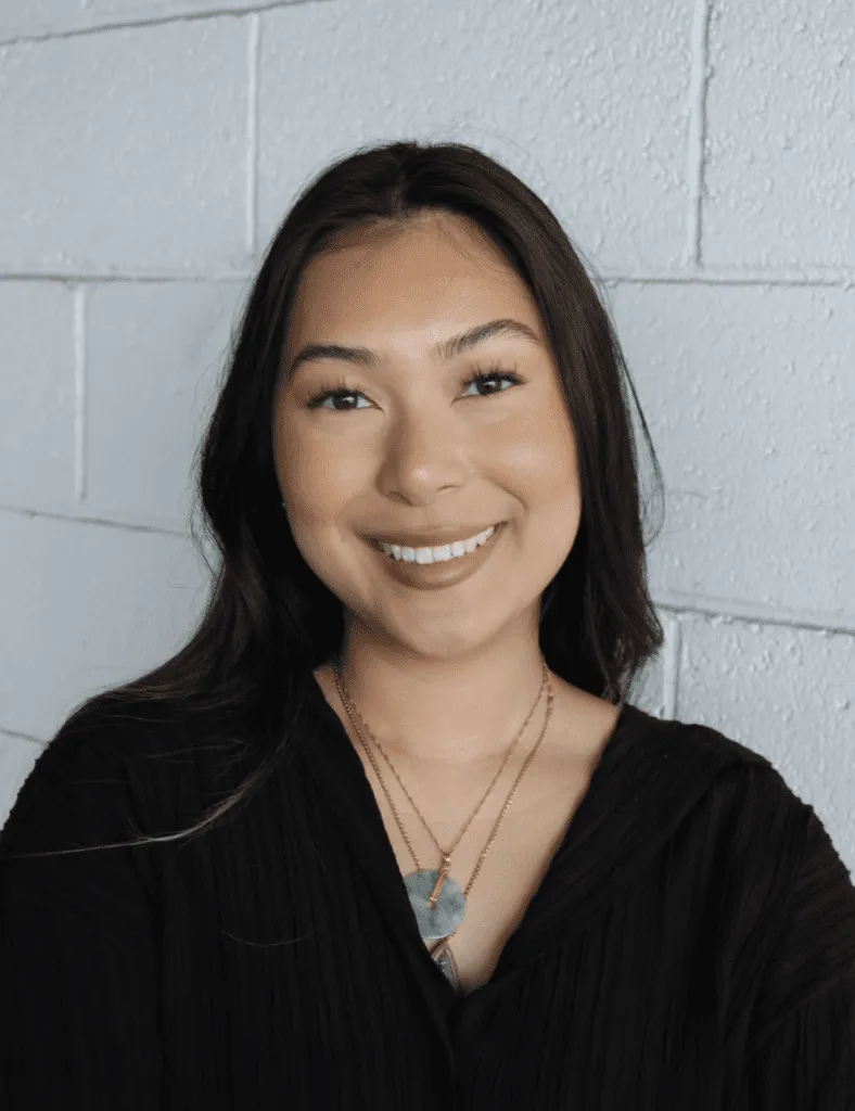 Smiling woman with long dark hair, wearing a black top and layered necklaces.