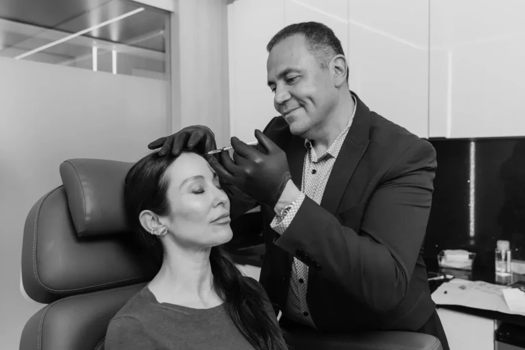 Plastic surgeon performing a cosmetic injection on a woman's forehead in a clinic setting.