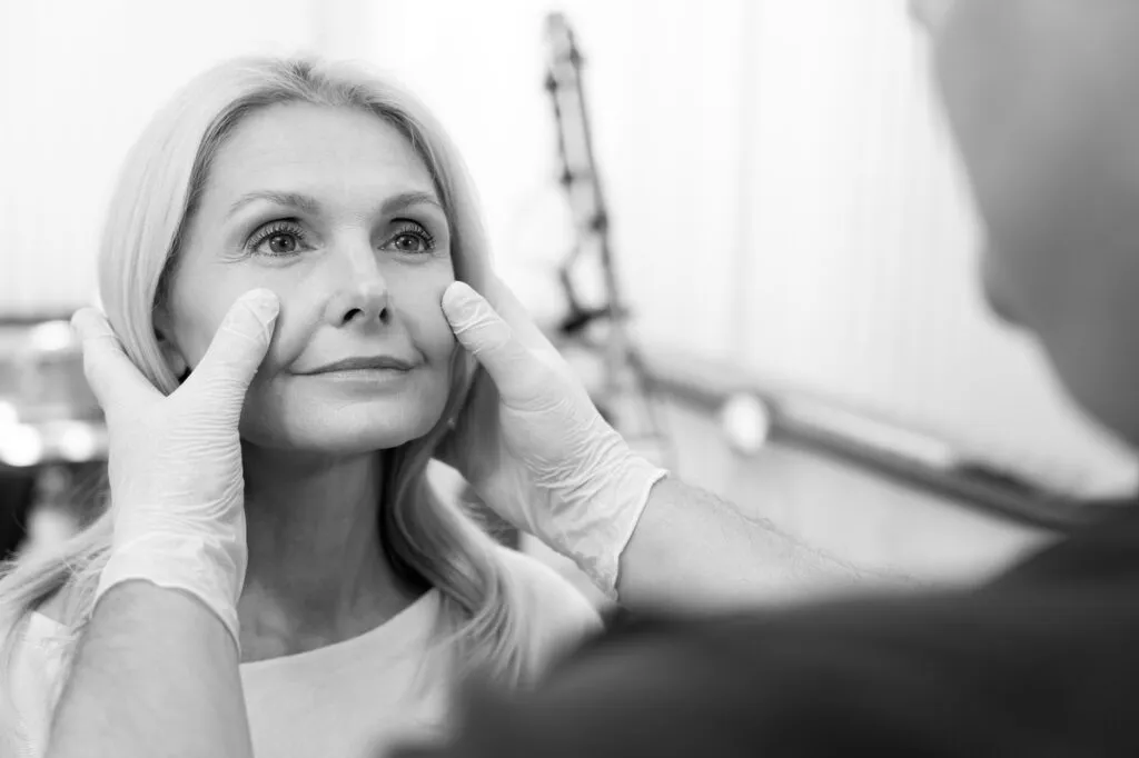 Doctor examining woman's face at plastic surgery consultation.