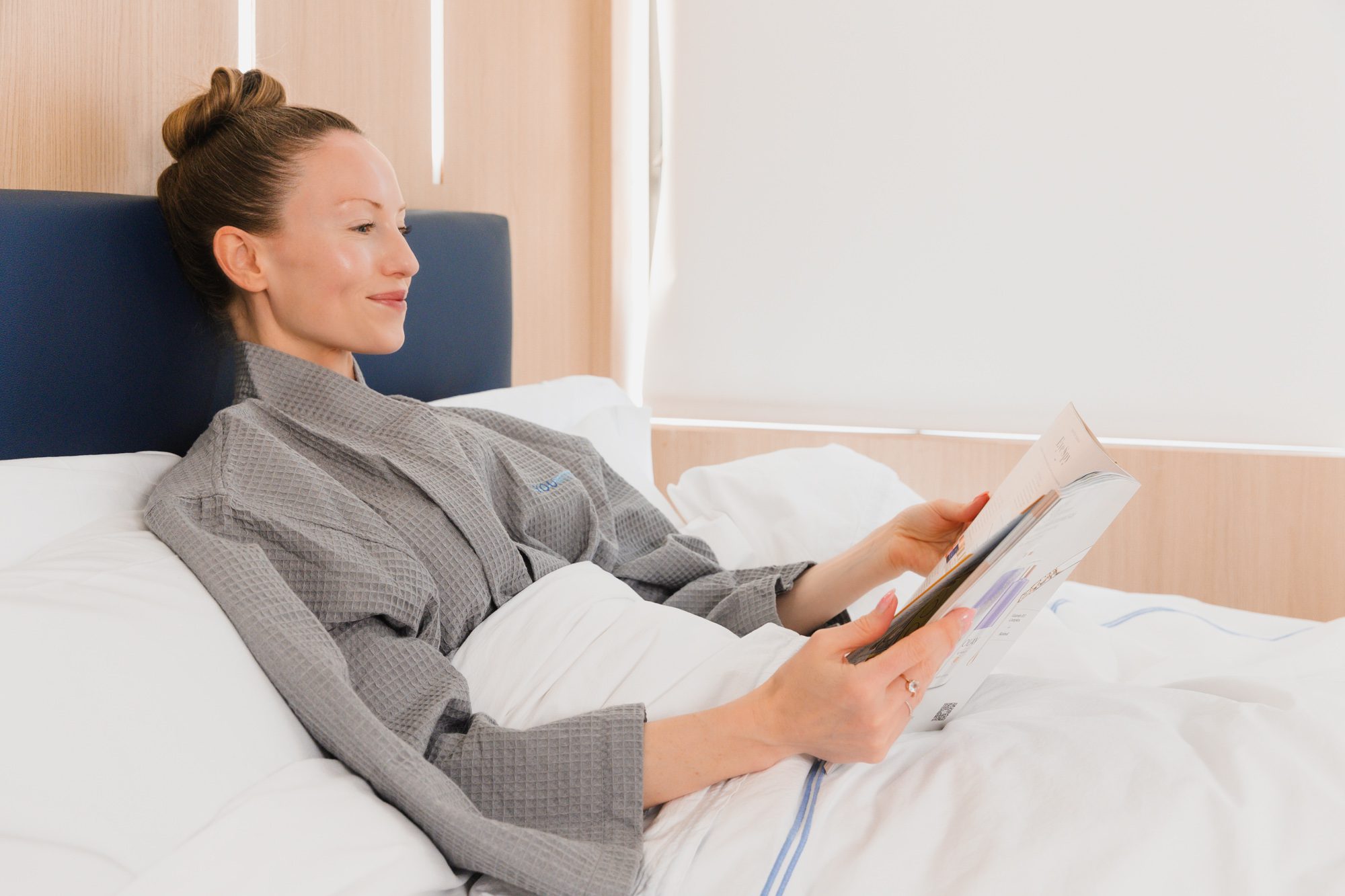 Woman in recovery at a plastic surgery center, relaxing and reading in bed.