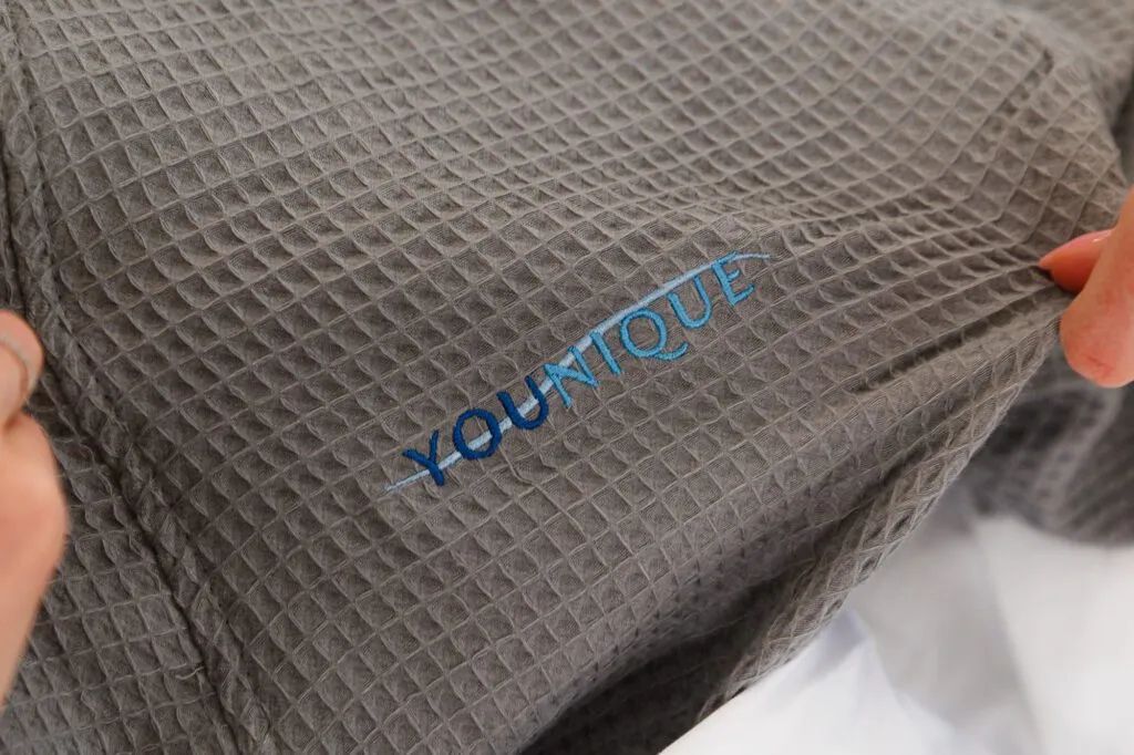 Gray fabric with "YOUNIQUE" embroidered, held by a hand.