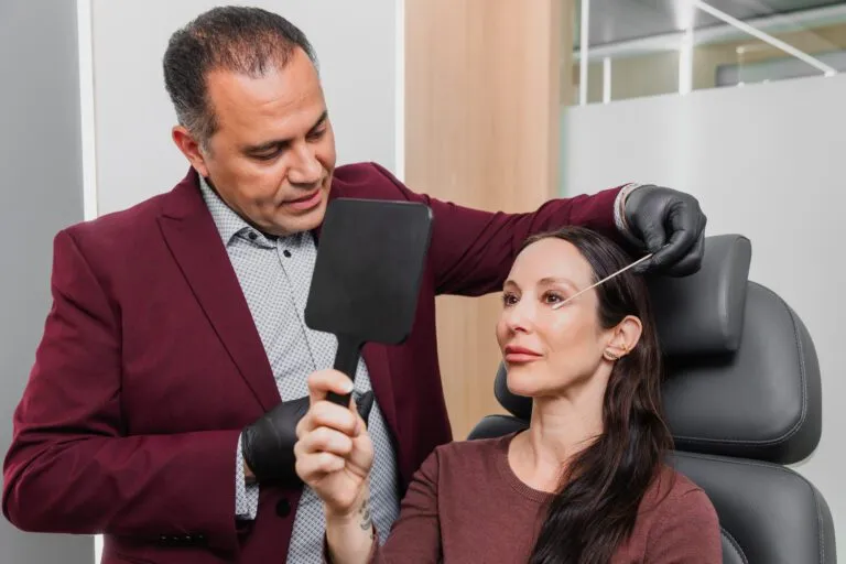 Plastic surgeon consulting with a patient examining her face using a mirror.
