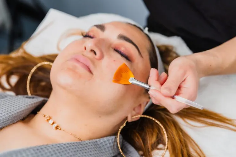 Woman receiving facial treatment with brush applicator at plastic surgery center.