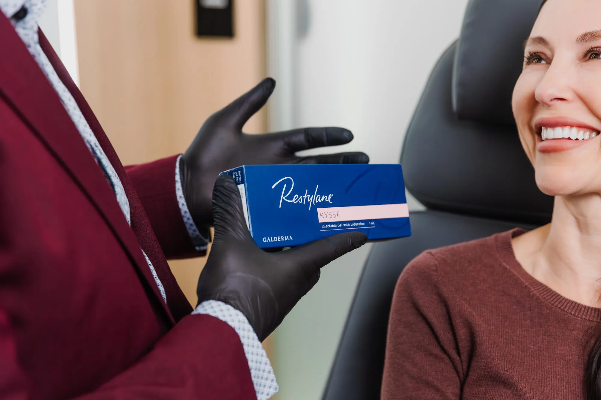 Plastic surgeon holding Restylane Kysse dermal filler package near smiling patient.