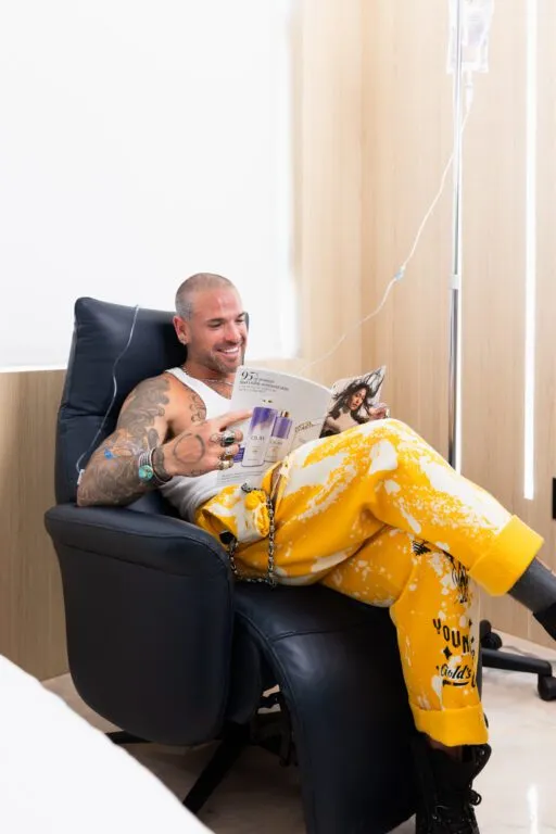 Man relaxing in a modern clinic chair, reading a magazine, receiving IV therapy.