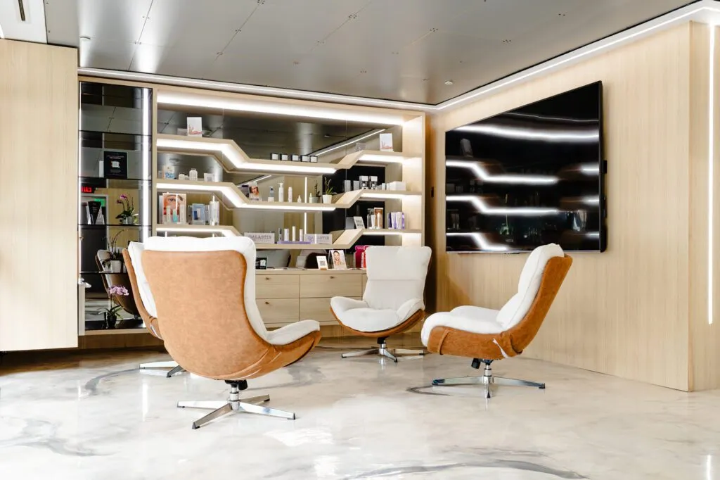 Modern waiting area with plush chairs, sleek shelving, and skincare products at a plastic surgery center.