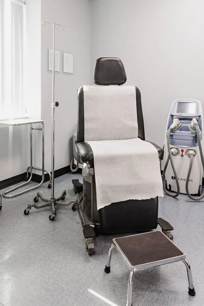 Modern plastic surgery consultation room with chair and medical equipment.