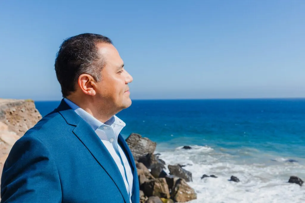 Man in a blue suit smiling by the ocean cliffs.