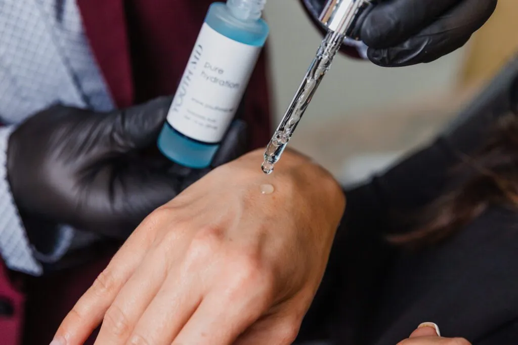 Gloved hand applying hydrating serum on skin with dropper.