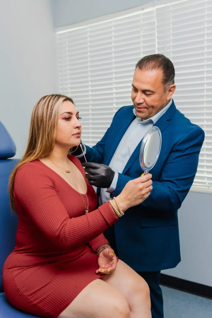 Plastic surgeon consulting with a patient holding a mirror in a clinic setting.