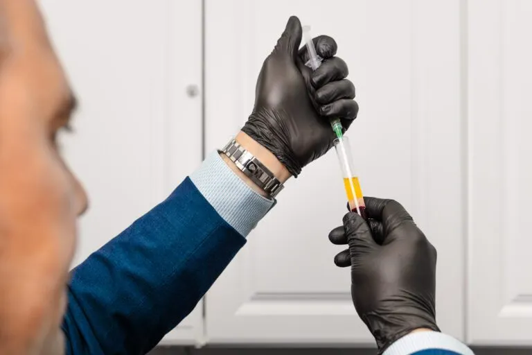 Doctor in blue suit preparing syringe with blood sample for procedure.