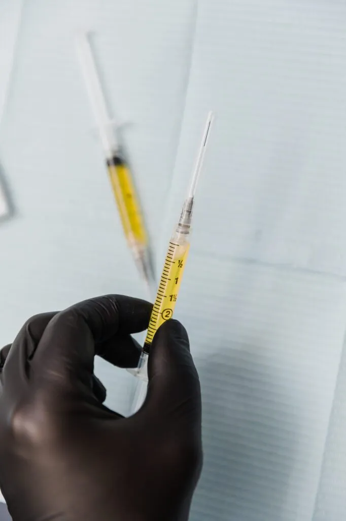 Gloved hand holding a syringe with yellow liquid, prepared for cosmetic procedure.