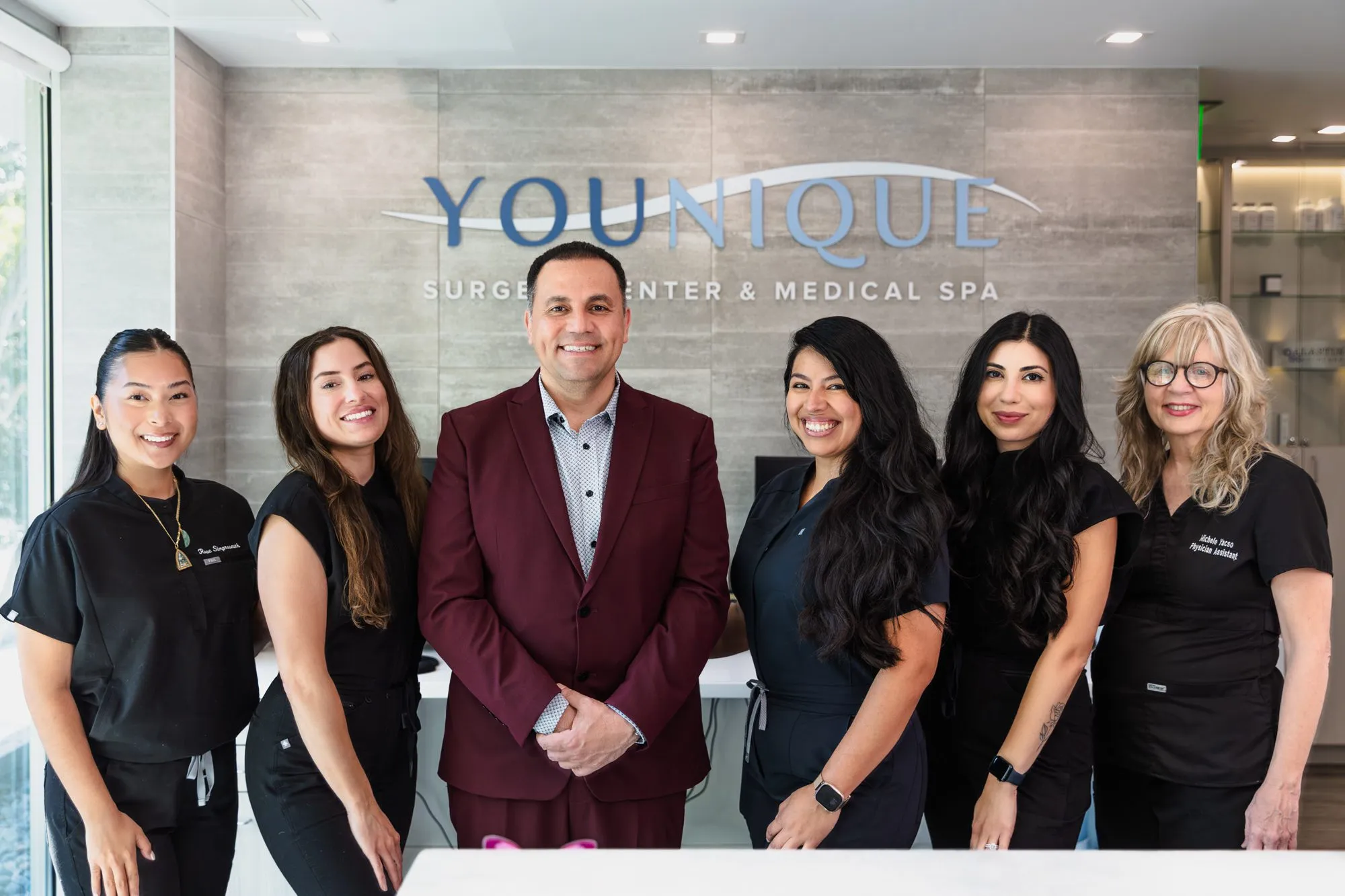A team of professionals at a plastic surgery center standing in front of the clinic sign.