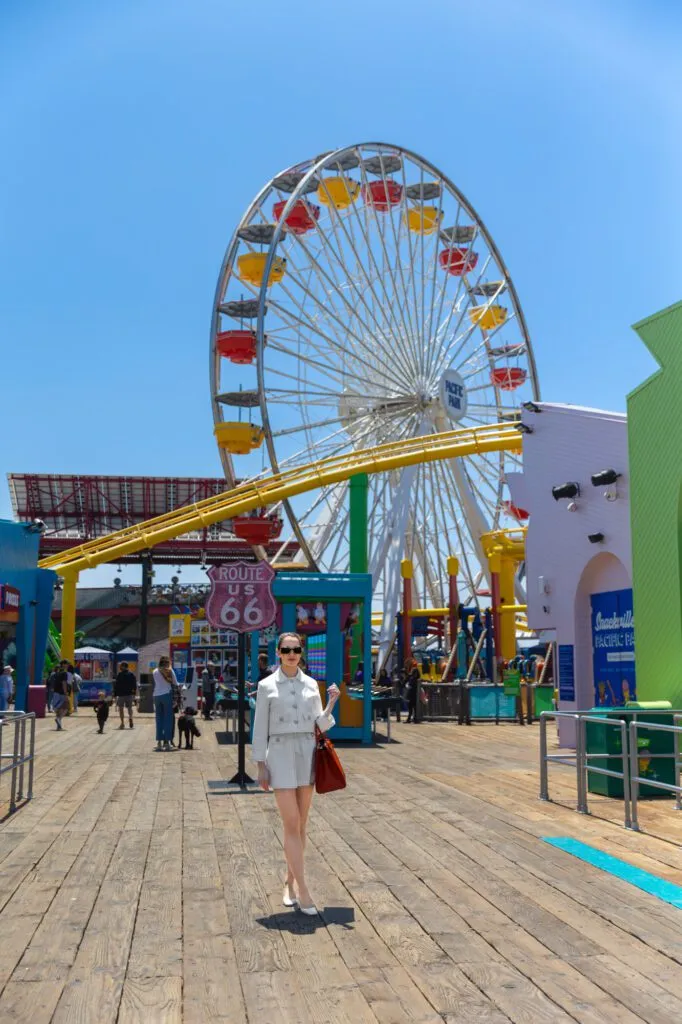 Woman walking on a boardwalk near a Ferris wheel, representing confidence and beauty.