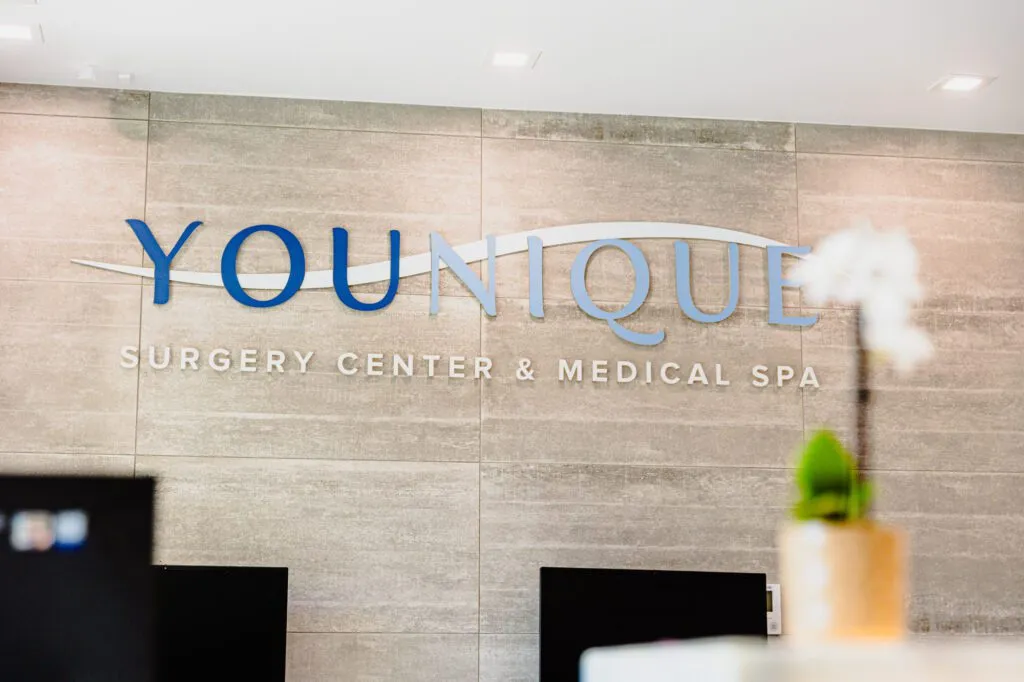 "Younique Surgery Center and Medical Spa logo on a modern interior wall."