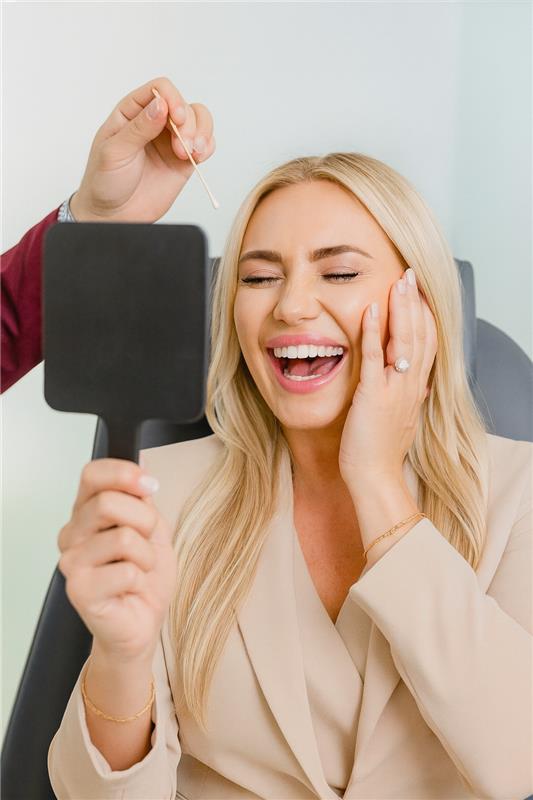Woman happily examining results in mirror at plastic surgery center.