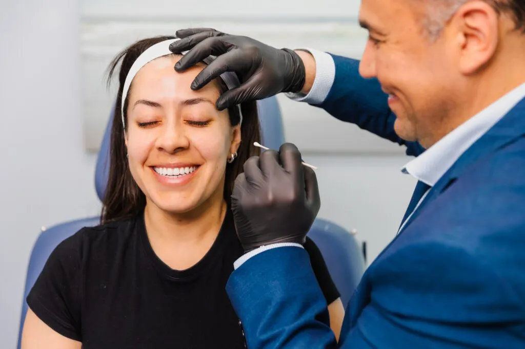 Patient smiling while receiving a skincare treatment at a plastic surgery center.