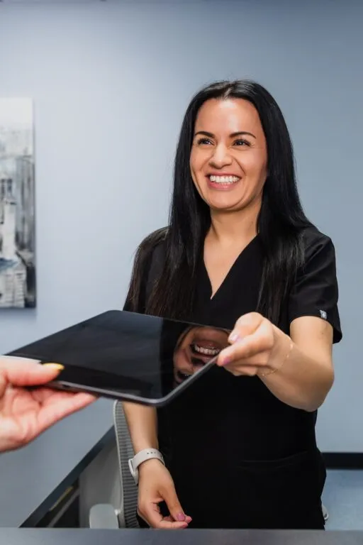 Smiling receptionist handing a tablet at a plastic surgery center.