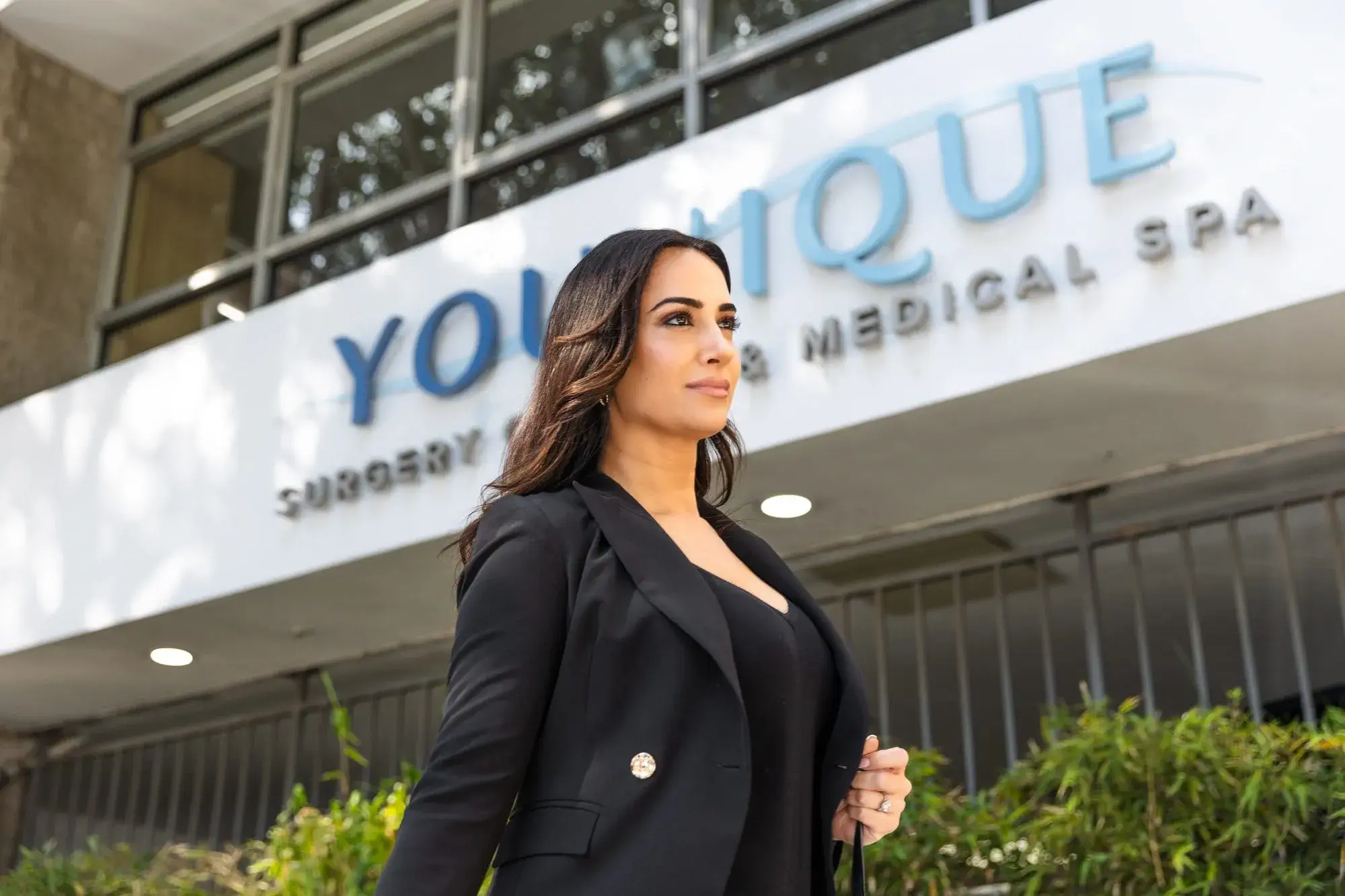 Businesswoman in a black suit standing confidently in front of a medical spa building.